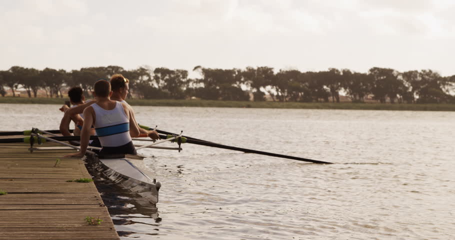 Rear view close up of three Caucasian male rowers, after a rowing practise, sitting in a boat by a jetty, talking and discussing, on a sunny day, in slow motion