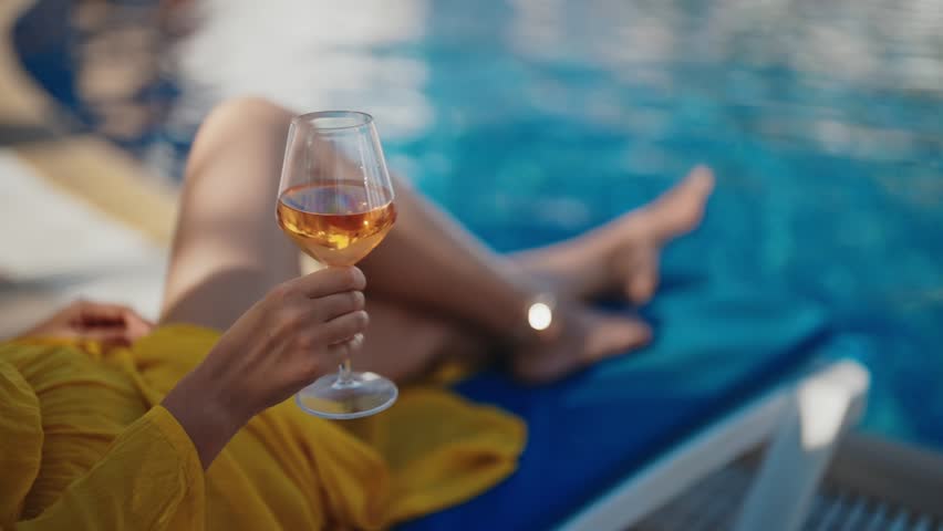 Woman with wine relaxing by the swimming pool.