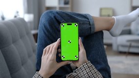 Girl using smartphone with green screen in living room watching movie, video content. Tracking markers. Indoors. Browsing social network, news. Internet surfing communication online. Tap on screen 4K
