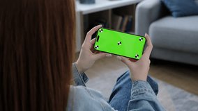 Woman using smartphone with horizontal green screen display watching movie, video content at home. Browsing social network, news. Girl using smartphone internet surfing communication online. Closeup