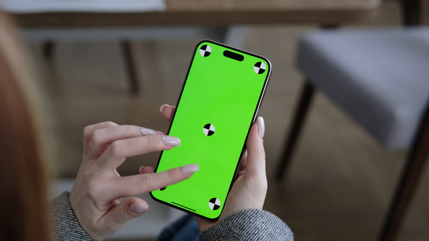 Woman using mobile phone vertical green screen. Female holding portable gadget close up indoors home living room. Mock-up for tracking. Browsing social network, news. Tap and scroll up