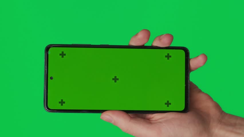 Male hand holding a smartphone with vertical green chroma key screen isolated on green background. Different signs and gestures with fingers. Technology and internet concept. Vertical video. Royalty-Free Stock Footage #3478823003