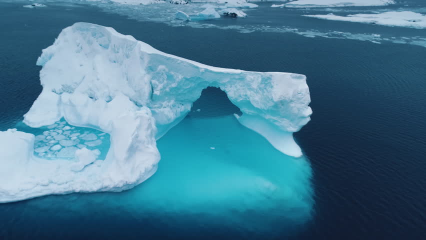 Big arctic iceberg arch melting ice underwater. Huge cracked glacier floating cold blue polar ocean. Natural beauty of towering glacier Antarctica. Cinematic ecology scene. Aerial drone shot panorama