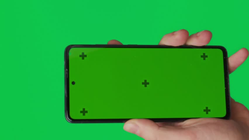 Male hand holding a smartphone with vertical green chroma key screen isolated on green background. Different signs and gestures with fingers. Technology and internet concept. Vertical video. Royalty-Free Stock Footage #3478825365