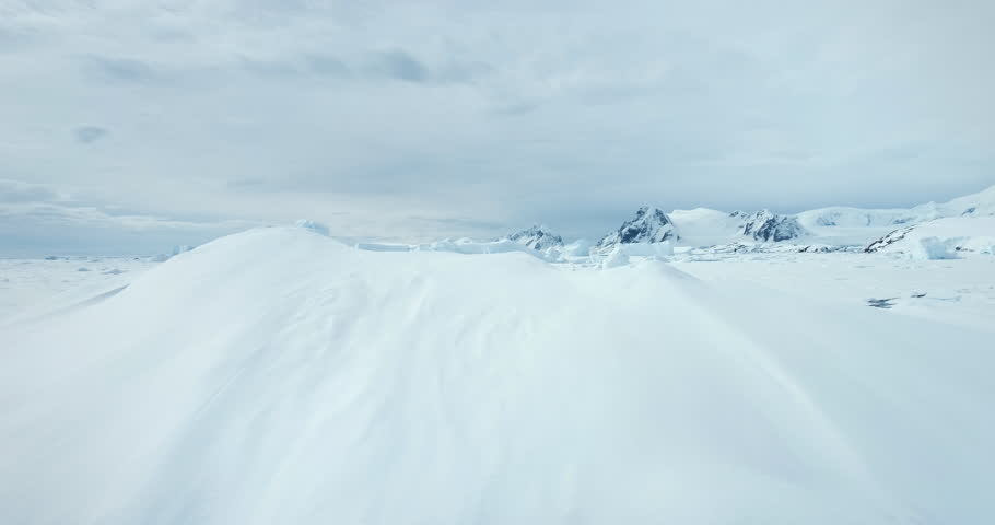 Fly over snow hill in Antarctica winter landscape. Frozen polar ocean with melted cracked river. Glacier and iceberg stuck in ice coast bay. Mountain range in background. Arctic travel and exploration