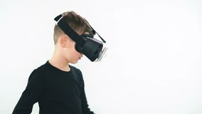 Little boy in virtual reality headset standing in white room and looking around in amazement, ten trying to touch something invisible