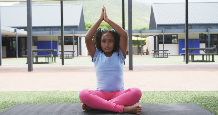 Biracial girl in a yoga pose at a school playground. She wears pink leggings and a blue top, promoting mindfulness and health in children, slow motion.