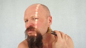 A man cuts his head with an electric razor. Hair care. Hairdresser. The bearded man shaves his head. Lumberjack. The guy's face and hand. Handsome male portrait. Barber - Powered by Shutterstock - Get 15% off with code: PIKWIZARD15