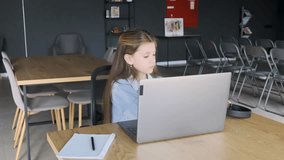 Distance learning. A young girl puts on wireless headphones while sitting in front of a laptop in a large auditorium.