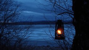 An old kerosene lantern hangs on a tree branch and burns with an orange flame. A lantern on the background of a gloomy natural landscape on the shore of the lake. Beauty is in nature. - Powered by Shutterstock - Get 15% off with code: PIKWIZARD15