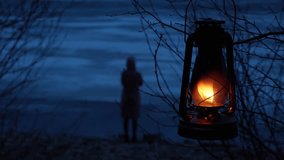 A burning kerosene lamp hanging on a tree branch, and the silhouette of a lonely girl standing in the gloomy darkness on the shore of a frozen lake. The harmony of nature and man. - Powered by Shutterstock - Get 15% off with code: PIKWIZARD15