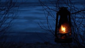 An old kerosene lantern hangs on a tree branch and burns with an orange flame. A lantern on the background of a gloomy natural landscape on the shore of the lake. Beauty is in nature. - Powered by Shutterstock - Get 15% off with code: PIKWIZARD15
