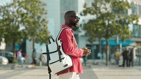 Cool young African Black man hipster student or tourist wearing sunglasses and backpack walking on city street outdoors holding smartphone using mobile cell phone technology device. - Powered by Shutterstock - Get 15% off with code: PIKWIZARD15