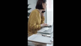 Professional woman multitasking with laptop and phone. Focused businesswoman attends to a call while working on her laptop in a modern office