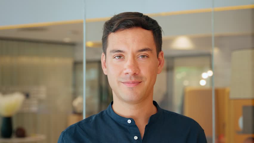Happy young latin business man leader or worker looking at camera standing in office. Smiling businessman manager, smiling professional employee or male entrepreneur, close up portrait.