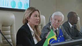 Female politician talking in microphone at table with EU and Brazilian flags while giving speech on international press conference - Powered by Shutterstock - Get 15% off with code: PIKWIZARD15