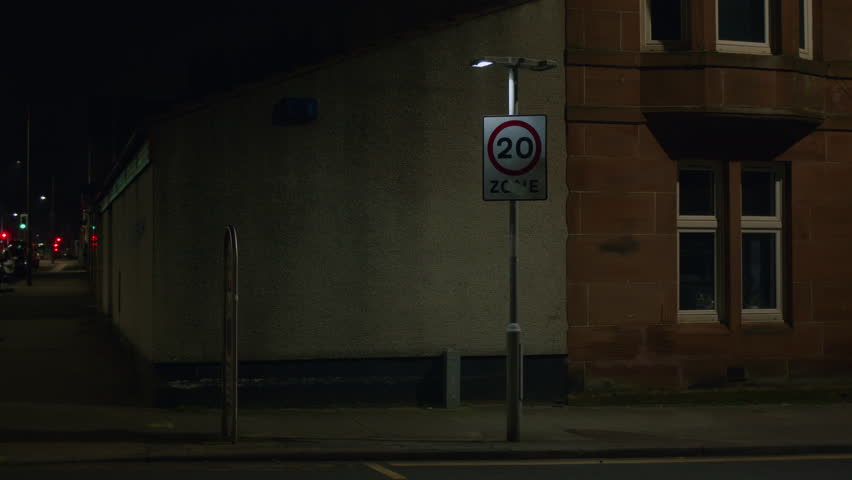 Faulty flashing 20 mph sign in empty street at night. Urban; town; city