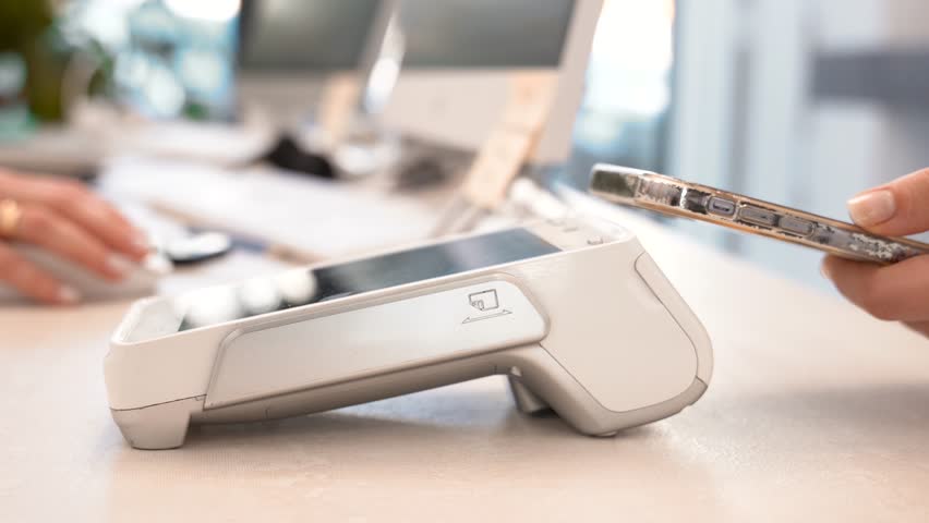 Pay by phone on electronic payment machine or card reader. E-money at cashless wallet. Female hand with pos-terminal and cellphone closeup. Client pays for the procedure in modern beauty clinic.