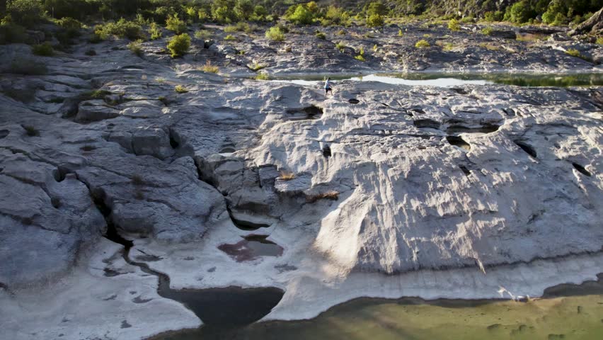 drone tracking person walking over rocks and water at state park during sunset