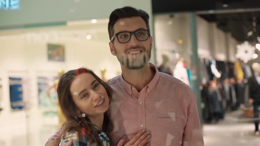 Young couple in shopping mall pausing to look at window display feel happy smiling talking shopper lockdown interior christmas love girl man together close up portrait slow motion