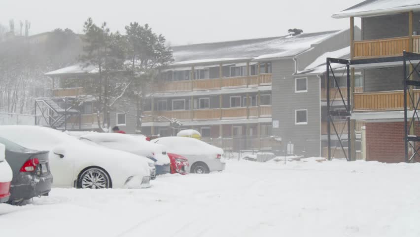 View of a snow storm covering cars and a parking lot near apartment buildings in Dartmouth, Canada. People go out into the street with shovels and shovel heaps of snow, digging cars out of the snow. 