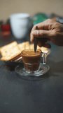 beautiful vertical video shot of a cup of coffee milk stirred in a white glass, with biscuits on the table