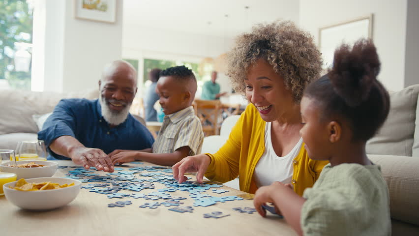 Grandparents with grandchildren indoors at home doing jigsaw puzzle together with parents in background - shot in slow motion