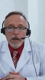 Portrait of a doctor in headset. Medical specialist giving a consultation online. Professional male physician in white medical uniform speaks looking at camera. Vertical video