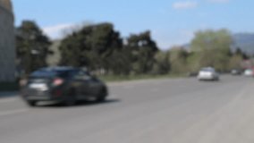 Defocused shot of cars driving along a highway with trees under the sunny sky.