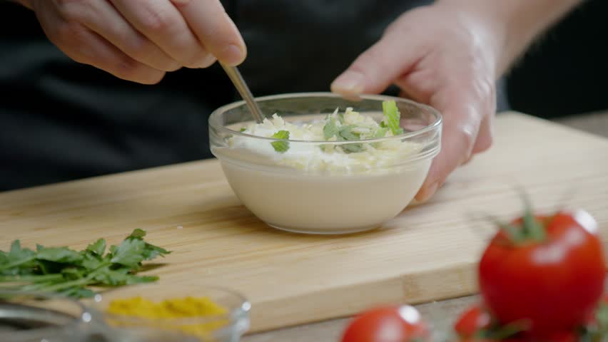 The chef mixes garlic and herbs with sour cream in a saucepan. They make a delicious white sauce, which is used in the restaurant kitchen to serve meat and fish dishes. Close up. Slow motion. 4k
