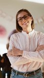 Vertical video portrait of a happy female teacher with a bob hairstyle in glasses with blue eyes in a pink shirt who smiles with her arms crossed on her chest and looks at the camera against the