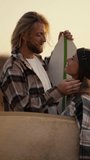 Vertical video: A blond guy with long hair with a beard in a checkered shirt stands close and communicates with his blonde girlfriend in a checkered shirt who looks at him and touches his hair with