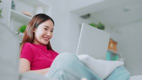 Happy young Asian woman using laptop while seated on couch at home