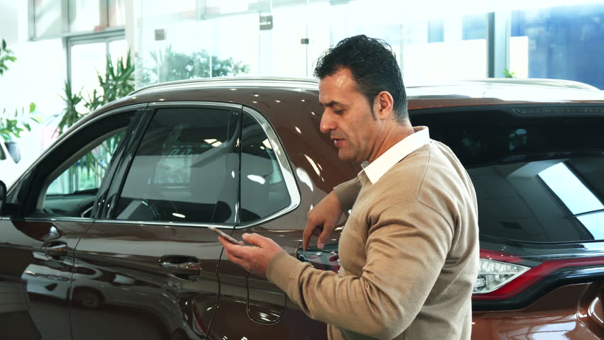 The man turns on the camera on the phone. He changes location several times and makes selfie. The man smiles widely and looks very pleased