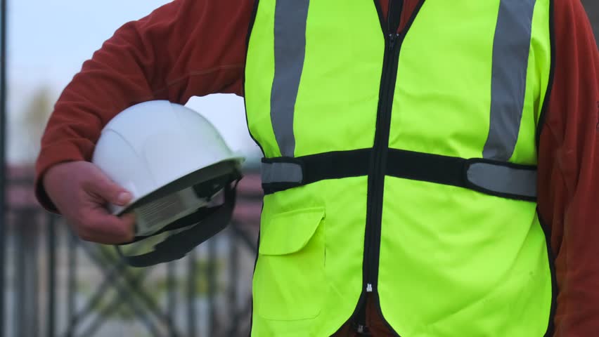 Builder safety helmet under his arm civil engineer standing in construction site, close up, protection and uniform. Slow motion.