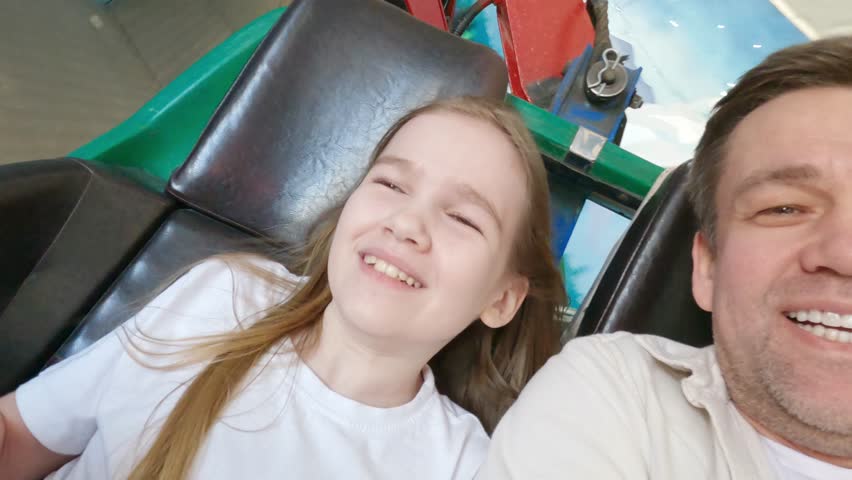 Dad and daughter go on thrill rides in an amusement park. Family outings and weekend fun. first person photography
