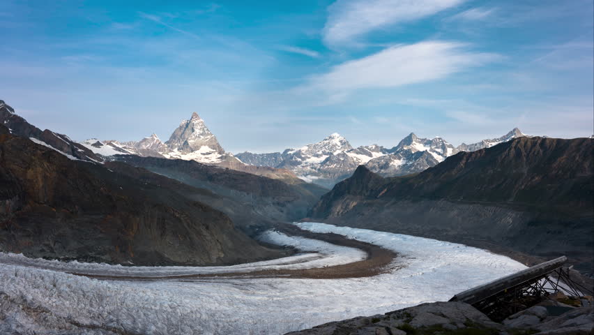 Matterhorn with snowy mountains and a glacier in the valley in time lapse during morning sunrise with bright blue sky and thin clouds in summer. Monte Rosa, Switzerland Royalty-Free Stock Footage #3479669923