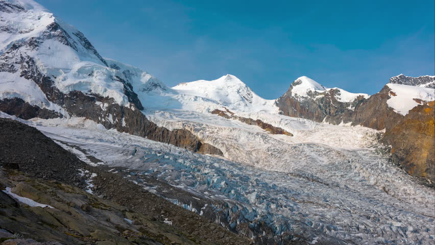 Snowy mountains with large glacier underneath in time lapse during sunrise with bright blue sky, near Monte Rosa, Switzerland	 Royalty-Free Stock Footage #3479670535