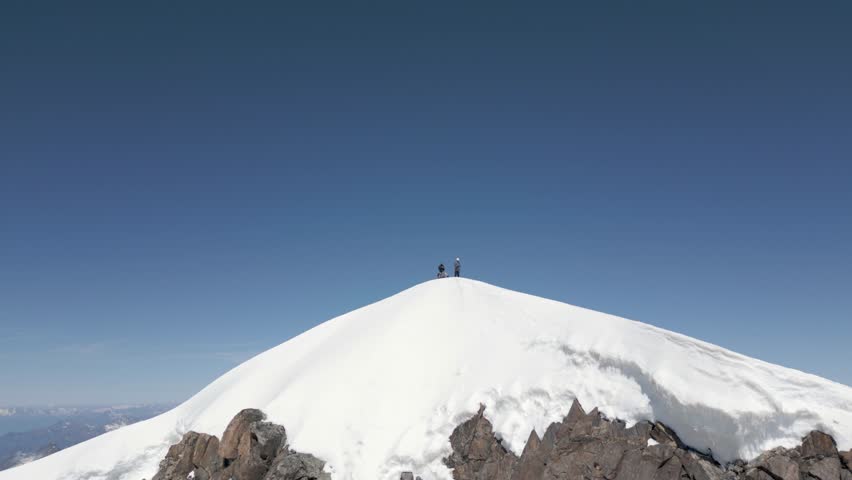two people climber alpinists standing on a high snowy mountain top during sunrise with bright blue sky, in Monte Rosa, Italy, Switzerland. Aerial drone landscape reveal Royalty-Free Stock Footage #3479670959