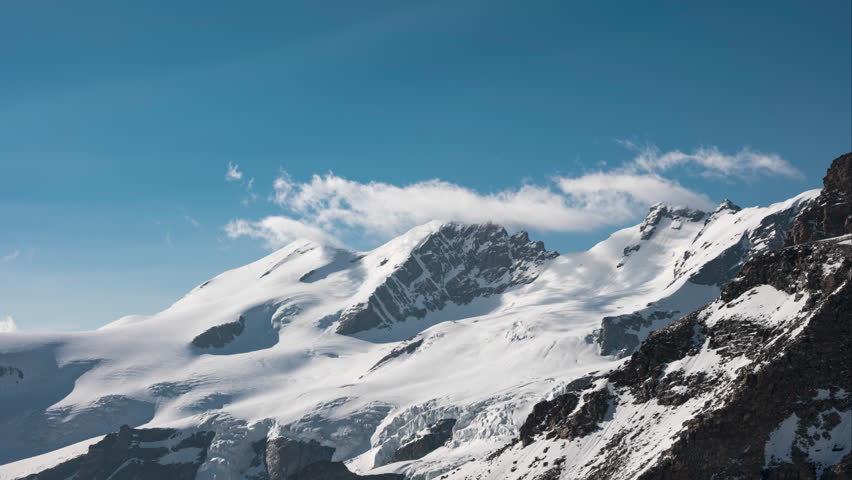 Thin clouds flying over snowy and rocky mountains alps in time lapse, during sunset with bright blue skies, in Breithorn, Monte Rosa, Italy	 Royalty-Free Stock Footage #3479678859
