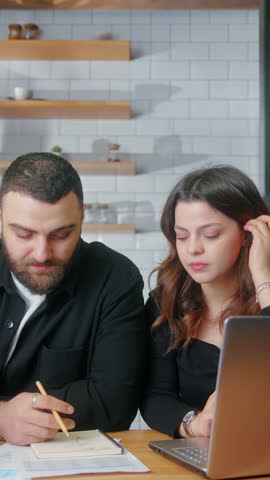 Vertical video. Young couple sit in the kitchen using laptop pay bills, use calculator count expenses, make budget control, manage finances, review overdue loan payments feel stressed