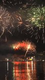 Bright fireworks exploding with colorful lights over sea shore and small mediterranean town. Vertical video