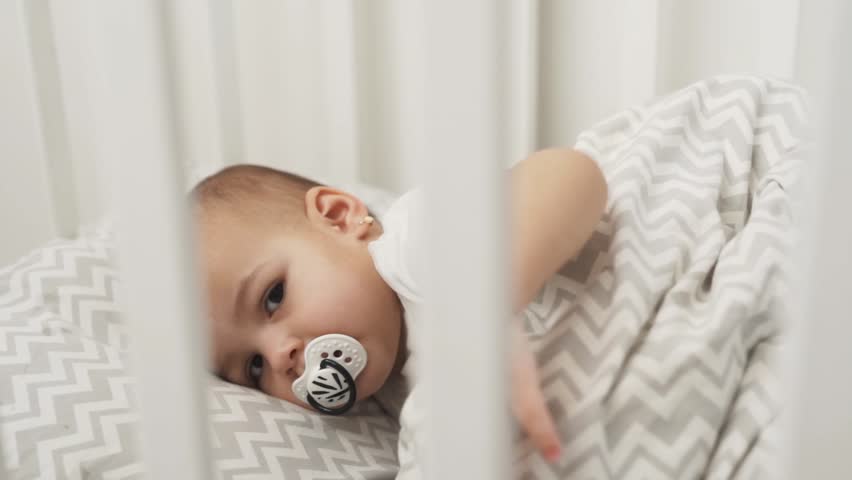 portrait of a baby girl falling asleep in a crib with a pacifier in her mouth Royalty-Free Stock Footage #3479810549