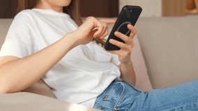 Close up video of young cheerful woman sitting on sofa and scrolling on smartphone