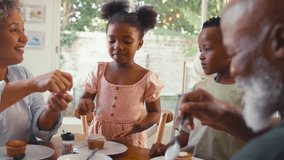 Grandparents with grandchildren indoors at home decorating cupcakes with icing and sprinkles together with parents in background - shot in slow motion - Powered by Shutterstock - Get 15% off with code: PIKWIZARD15