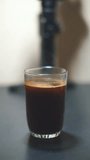 beautiful vertical video shot of a cup of black coffee being stirred in a white glass cup on a table