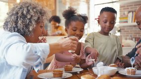 Grandparents with grandchildren indoors at home decorating cupcakes with icing and sprinkles together with parents in background - shot in slow motion - Powered by Shutterstock - Get 15% off with code: PIKWIZARD15