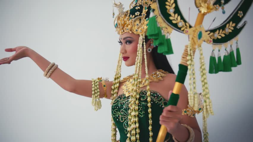 Woman in traditional Balinese dancer costume with golden headdress and green outfit, performing with elegant hand gesture during the daylight