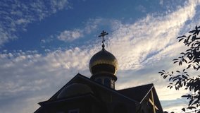 A church steeple with a cross on top of it. The sky is cloudy and the sun is setting. Close-up Footage