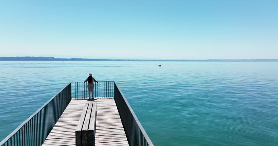 A woman stands on pier by the water, gazing at the horizon in leisure